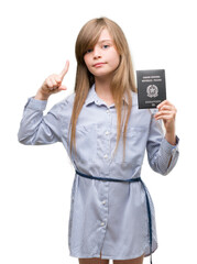 Wall Mural - Young blonde toddler holding italian passport surprised with an idea or question pointing finger with happy face, number one