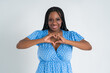 Happy plus size female model posing in blue dress on white background and showing heart sign, young African woman with curvy figure and pigtailed hairstyle, afro braids