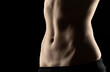 © vladimirfloyd - Close-up of a fit woman's stomach under the glow of light in a dark background