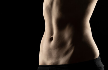 Close-up of a fit woman's stomach under the glow of light in a dark background