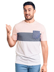 Wall Mural - Young handsome man wearing casual clothes smiling with happy face looking and pointing to the side with thumb up.