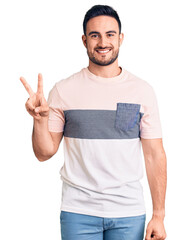 Wall Mural - Young handsome man wearing casual clothes showing and pointing up with fingers number two while smiling confident and happy.
