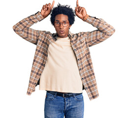 Canvas Print - Handsome african american man with afro hair wearing casual clothes and glasses doing funny gesture with finger over head as bull horns