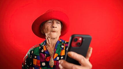 Wall Mural - Portrait of toothless elderly senior old woman with wrinkled skin looking at phone having great happy success winner isolated on red background. People emotions concept.