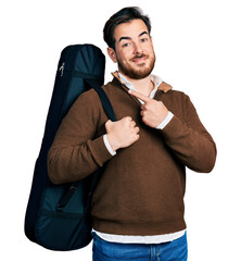 Wall Mural - Young hispanic man wearing guitar case smiling happy pointing with hand and finger