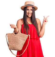 Poster - Young beautiful brunette woman wearing summer hat and dress holding bag smiling happy pointing with hand and finger to the side