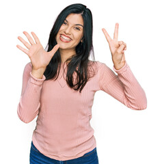 Wall Mural - Young hispanic woman wearing casual clothes showing and pointing up with fingers number seven while smiling confident and happy.