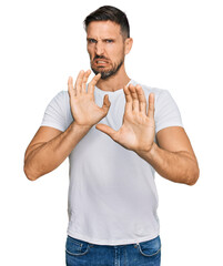 Wall Mural - Handsome man with beard wearing casual white t shirt disgusted expression, displeased and fearful doing disgust face because aversion reaction. with hands raised