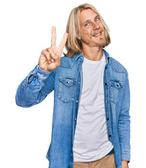 Canvas Print - Caucasian man with blond long hair wearing casual denim jacket smiling looking to the camera showing fingers doing victory sign. number two.