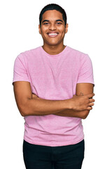 Wall Mural - Young handsome hispanic man wearing casual pink t shirt happy face smiling with crossed arms looking at the camera. positive person.