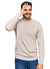 Wall Mural - Young hispanic man wearing casual clothes doing ok gesture with hand smiling, eye looking through fingers with happy face.