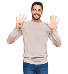 Wall Mural - Young hispanic man wearing casual clothes showing and pointing up with fingers number nine while smiling confident and happy.