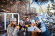 © Davor - Group of friends taking a selfie in winter outfits with coffee mugs outside a cabin