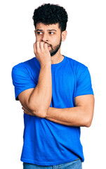 Canvas Print - Young arab man with beard wearing casual blue t shirt looking stressed and nervous with hands on mouth biting nails. anxiety problem.