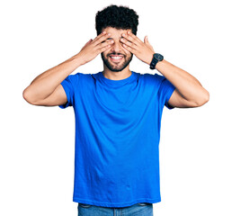 Canvas Print - Young arab man with beard wearing casual blue t shirt covering eyes with hands smiling cheerful and funny. blind concept.