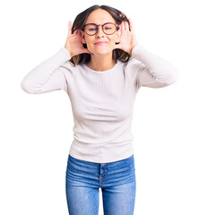 Wall Mural - Beautiful brunette young woman wearing casual white sweater and glasses trying to hear both hands on ear gesture, curious for gossip. hearing problem, deaf