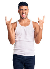 Sticker - Young hispanic man wearing casual clothes shouting with crazy expression doing rock symbol with hands up. music star. heavy concept.