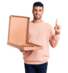 Poster - Young hispanic man holding delivery pizza box surprised with an idea or question pointing finger with happy face, number one