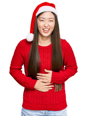 Sticker - Young chinese woman wearing christmas hat smiling and laughing hard out loud because funny crazy joke with hands on body.