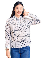 Sticker - Young beautiful chinese woman wearing casual shirt smiling doing phone gesture with hand and fingers like talking on the telephone. communicating concepts.