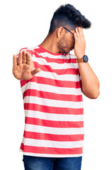 Wall Mural - Handsome latin american young man wearing casual clothes and glasses covering eyes with hands and doing stop gesture with sad and fear expression. embarrassed and negative concept.