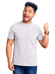 Sticker - Handsome latin american young man wearing casual tshirt smiling with happy face looking and pointing to the side with thumb up.