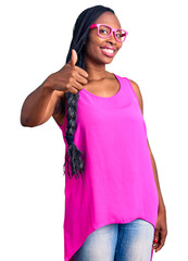 Sticker - Young african american woman wearing casual clothes and glasses doing happy thumbs up gesture with hand. approving expression looking at the camera showing success.