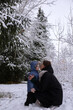 © Vladyslav - Mom with daughter in winter snowy forest. Mom kisses her daughter and warms her hands with her breath. Young girl with her daughter walking in the forest in winter.