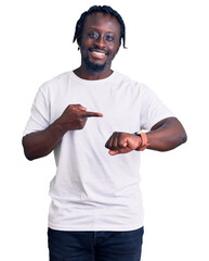 Poster - Young african american man with braids wearing casual white tshirt in hurry pointing to watch time, impatience, upset and angry for deadline delay