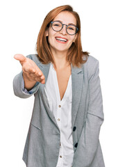 Poster - Young caucasian woman wearing business style and glasses smiling friendly offering handshake as greeting and welcoming. successful business.