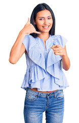 Wall Mural - Young beautiful latin girl wearing casual clothes smiling doing talking on the telephone gesture and pointing to you. call me.