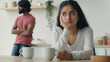 Upset Indian woman wife thinking of relationship problems after quarrel with husband on kitchen offended man stand background. Married diverse multiracial couple arguing having conflict disagreement