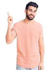 Wall Mural - Young handsome man with beard wearing casual t-shirt with a big smile on face, pointing with hand and finger to the side looking at the camera.