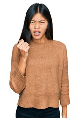 Canvas Print - Beautiful young asian woman wearing casual winter sweater angry and mad raising fist frustrated and furious while shouting with anger. rage and aggressive concept.