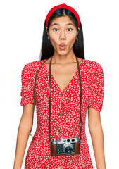 Sticker - Beautiful young asian woman wearing dress and vintage camera scared and amazed with open mouth for surprise, disbelief face