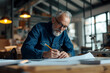 © v.senkiv - Portrait of a mature male architect working in an office at a desk, studying plans for a new building