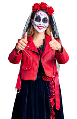 Canvas Print - Woman wearing day of the dead costume over background approving doing positive gesture with hand, thumbs up smiling and happy for success. winner gesture.