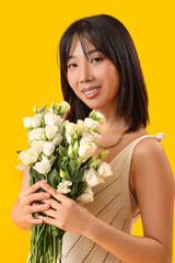 Poster - Beautiful Asian woman holding bouquet of eustoma flowers on yellow background