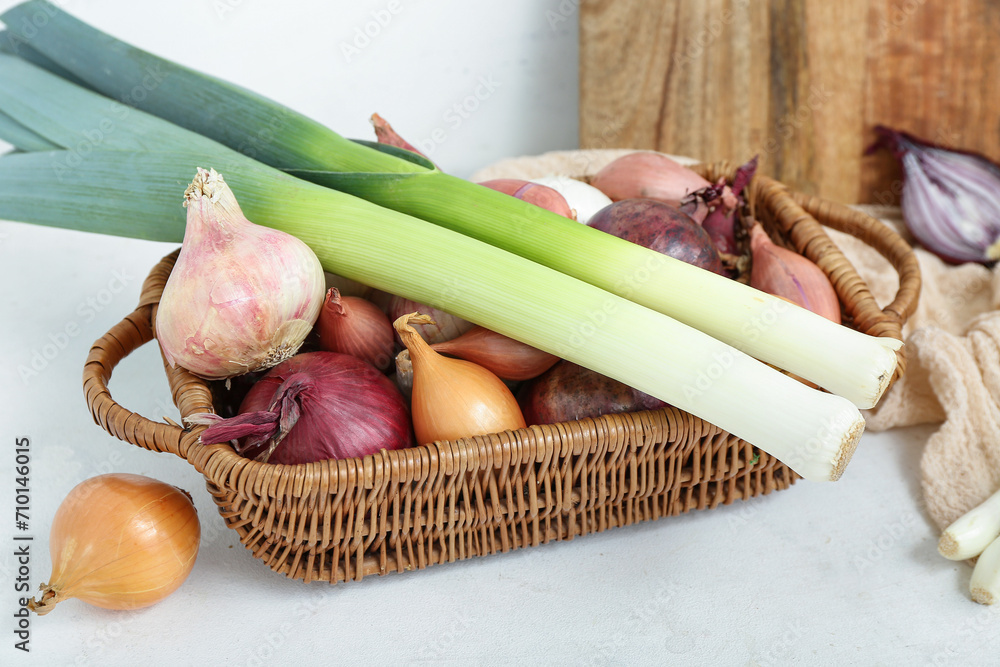 Wicker basket with different kinds of onion on light background, closeup