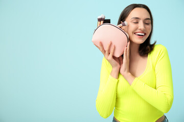 Sticker - Beautiful young woman with cosmetic bag full of makeup products on blue background