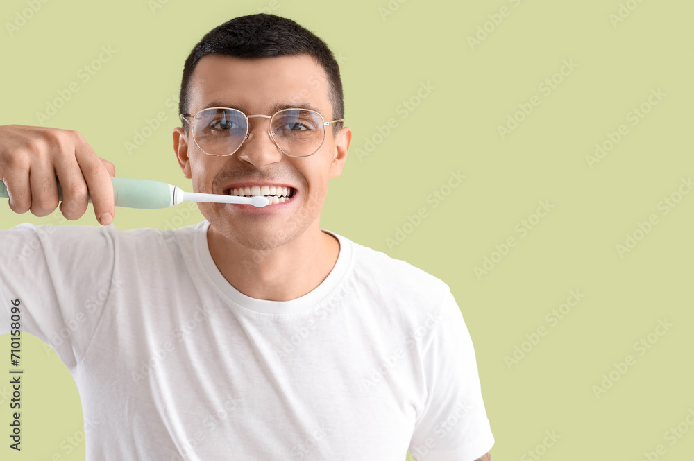 Handsome young man with electric tooth brush on green background. Dental care concept
