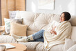 © Pixel-Shot - Young Asian woman with warm plaid sitting on sofa at home