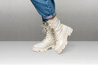 Female legs in white combat boots and blue jeans stand on white background, side view. Woman wearing trendy military beige shoes on high platform with laces. Seasonal female fashion