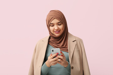 Sticker - Beautiful young Muslim woman in hijab with mobile phone on pink background