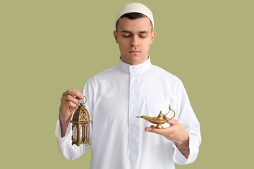 Wall Mural - Young Muslim man with lamps on green background. Ramadan celebration