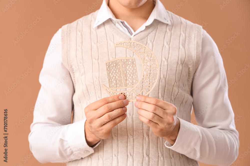 Young Muslim man with decorative crescent on beige background, closeup. Ramadan celebration