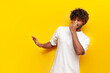 © Богдан Маліцький - young curly indian man showing disgust and covering his nose with hand on yellow isolated background, guy refuses bad smell and rejects stench