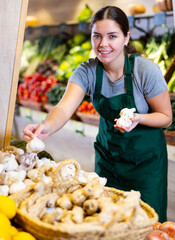 Wall Mural - Woman seller wearing apron arranges garlic and other vegetables on the counter and display case