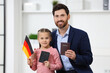 Immigration. Happy man with his daughter holding passports and flag of Germany indoors