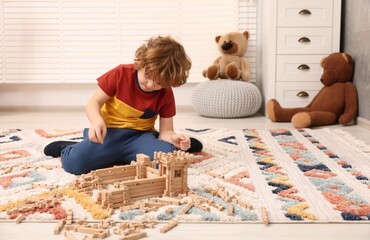 Sticker - Little boy playing with wooden construction set on carpet in room, space for text. Child's toy